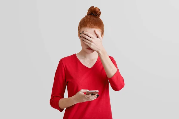 Portrait de belle jeune femme taches de rousseur couvre le visage avec la main, utilise le téléphone mobile moderne pour la communication en ligne, isolé sur fond de studio blanc. Concept de technologie et de personnes — Photo