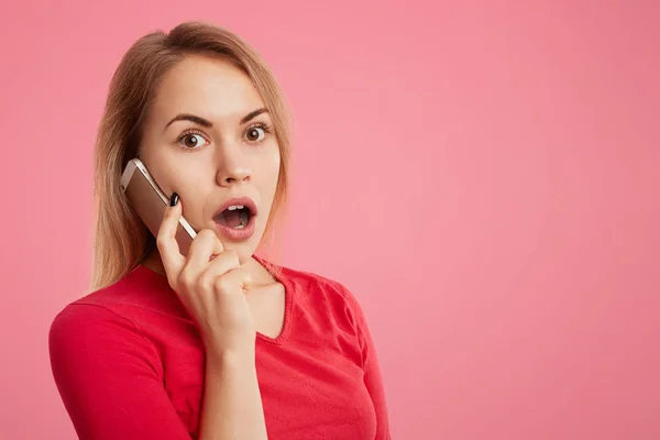 Choqué jeune femme perplexe a conversation téléphonique par téléphone, surpris d'entendre des nouvelles inattendues, isolé sur fond rose avec de l'espace de copie pour votre publicité ou texte promotionnel . — Photo