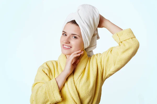 Vacker kvinna klädd i gul badrock och handduk på huvudet, kommer från badrum, demonstates sin ren frisk hud, åtnjuter tar dusch, utgör mot vit bakgrund. Skönhet och välbefinnande koncept — Stockfoto