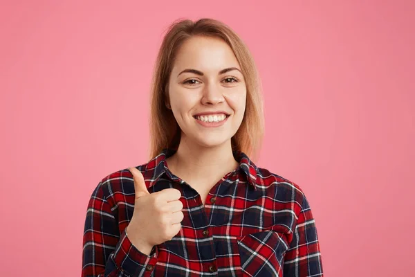 快乐的微笑的年轻女性举起拇指, 展示喜欢的标志, 赞许的东西, 表明她是满意的, 在良好的心情, 手势室内反对粉红色工作室背景 — 图库照片