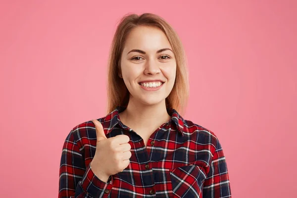 Feliz sonrisa joven hembra levanta el pulgar hacia arriba, demuestra como signo, aprueba algo, muestra que ella está satisfecha con ella, estar de buen humor, gestos en interiores contra de fondo de estudio rosa — Foto de Stock