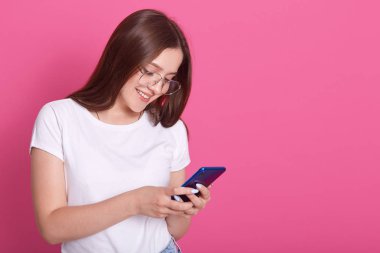 Arkadaşlarına ya da kocasına mesaj yazan sevimli bir kadının portresini yakından çek. Genç bir bayan cep telefonu tutuyor ve pembe arka planda dururken gülümsüyor. Modern teknoloji kavramı.