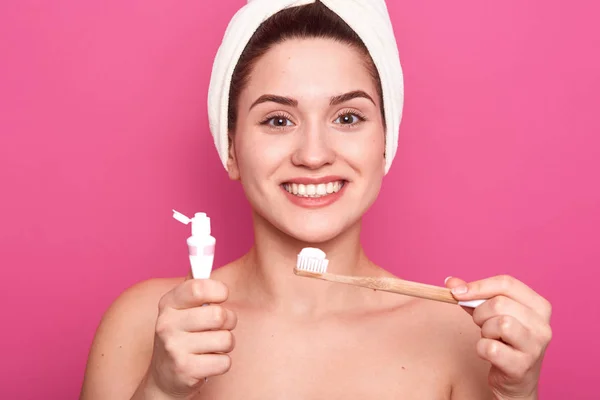 Foto de estudio de una joven guapa sosteniendo cepillo y pasta de dientes para la limpieza de dientes en las manos. chica sonriente feliz con cepillo de dientes, aislado sobre fondo de estudio rosa. Concepto de higiene oral . — Foto de Stock
