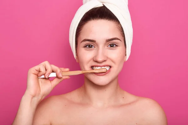 Primer plano retrato de atractiva joven caucásica sonriente mujer aislada sobre fondo de estudio rosa, guapa hembra cepillándose los dientes, mirando a la cámara con encantadora sonrisa. Concepto de higiene oral . —  Fotos de Stock