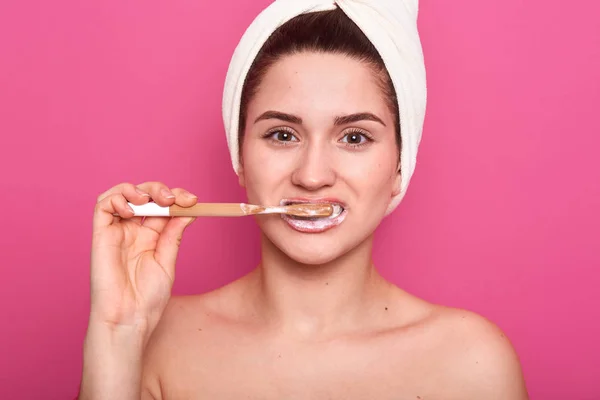 Close-up portretvan jonge glimlachende vrouw die haar tanden schoonmaakt met tandenborstel in de badkamer, staat met witte handdoek en ontbloot schouders, aantrekkelijke vrouw die 's ochtends ingrepen doet. Mondelinge hygiëne. — Stockfoto