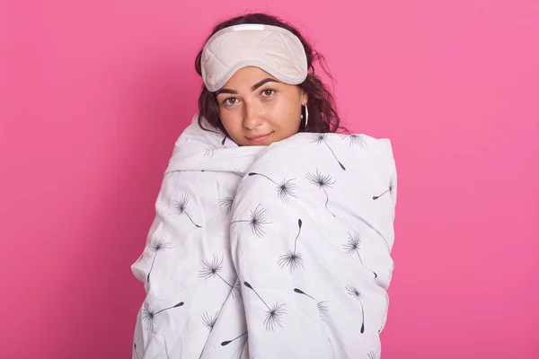 Close up portrait of smiling brunette woman waking up portrait with blanket and blindfold eyes mask for sleep on forehead, charming female posing isolated over pink studio background. Morning concept. — Stock Photo, Image