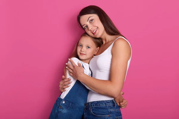 Feliz bela jovem mãe abraçando sua pequena filha alegre, mulher attarctive posando com sua encantadora criança loira fêmea isolada sobre o fundo do estúdio rosa, senhoras expressando amor . — Fotografia de Stock