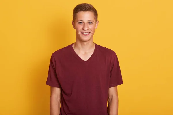 Primer plano retrato de chico joven complacido vestido camiseta casual marrón, mirando sonriendo a la cámara, expresa felicidad, modelo posando aislado sobre fondo amarillo. Concepto de gente, juventud y estilo de vida . —  Fotos de Stock