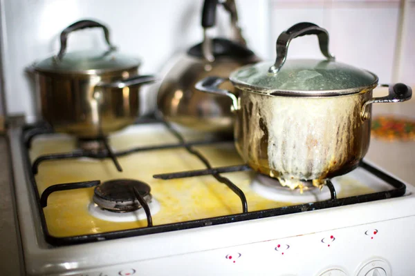 Indoor shot of pot with ran away porridge on stove, kettle and pots on gas cooker, dirty pot on muddy gas stove, preparing porrige for breakfast for liitle baby, milk porrige run away. Eating concept. — Stock Photo, Image