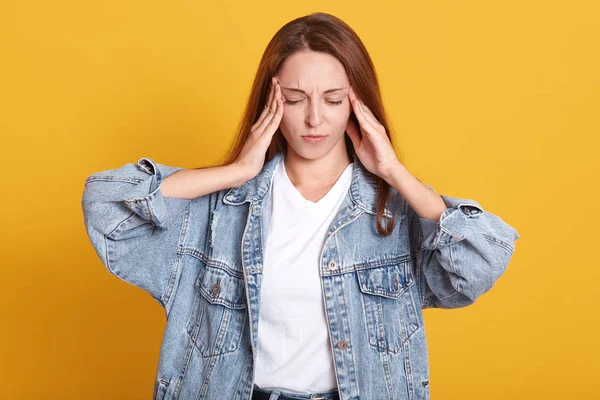 Image d'une jeune femme contrariée et agacée gardant les mains sur les tempes, ayant mal à la tête, souffrant de douleur, fermant les yeux, ayant une expression faciale désagréable. Concept des personnes et des problèmes de santé . — Photo