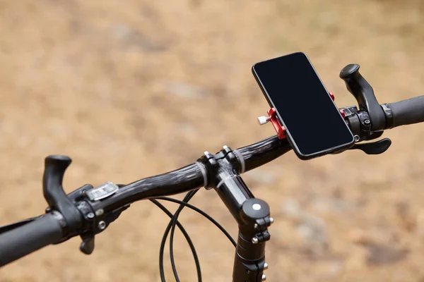 Black handlebar of sport bicycle over forest road background, having smartphone attached to right side, movement along road, gps navigator, going according to online map. Orientation concept. — Stock Photo, Image