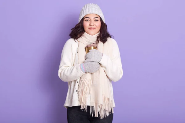漂亮的姑娘拿着热杯子洗手，喜欢在寒冷的冬季喝热茶或咖啡，穿上暖和的毛衣、围巾、手套和帽子，在紫色的背景下显得孤立无援. — 图库照片