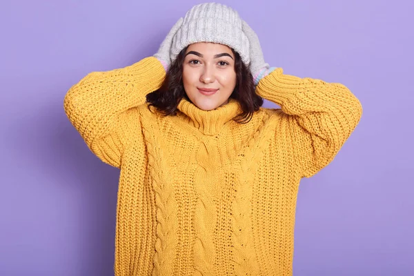 Potret wanita langsing yang menawan mengenakan sweater kuning dan topi putih, terlihat rapi, wanita kaukasia menyamar dengan senyum tulus dan menjaga tangannya di kepala, melihat langsung ke kamera . — Stok Foto