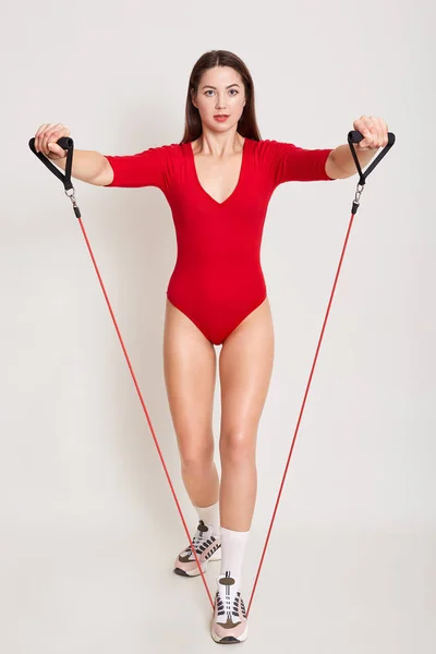 スタイリッシュな赤のコンビを身に着けている若いブルネットの女性の完全な長さの写真、魅力的な女性は白いスタジオの背景に隔離されたポーズで、拡大して彼女の足を伸ばします。スポーツと健康的なケアの概念 — ストック写真