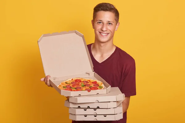 Foto de un hombre feliz y alegre con una camiseta casual borgoña, mirando sonriente a la cámara y sosteniendo cajas de pizza, se abrió la caja superior de keppeng, posando aislado sobre un fondo amarillo. Concepto de entrega . — Foto de Stock