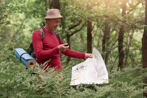 Koordinace a navigace v lese. Obrázek muže držícího v rukou kompas a papírovou mapu, nacházejícího správnou cestu ve dřevě, který se ztrácí při chůzi po stezce a vychutnávajícího si krásnou přírodu. — Stock fotografie