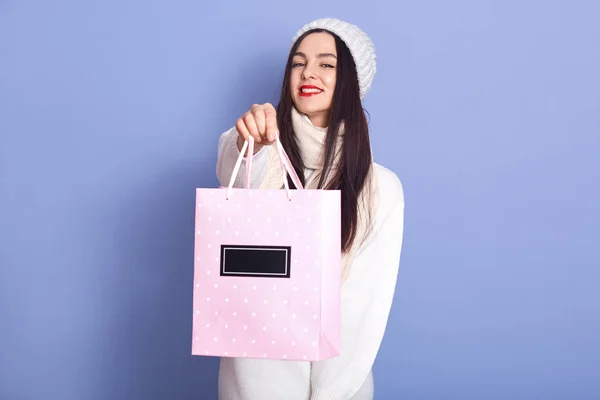 Retrato de hermosa mujer agradable sosteniendo bolsa de papel rosa con la compra, mirando directamente a la cámara, tener el pelo largo y negro, pasar tiempo solo, disfrutar de las vacaciones de invierno. Concepto de compras . — Foto de Stock