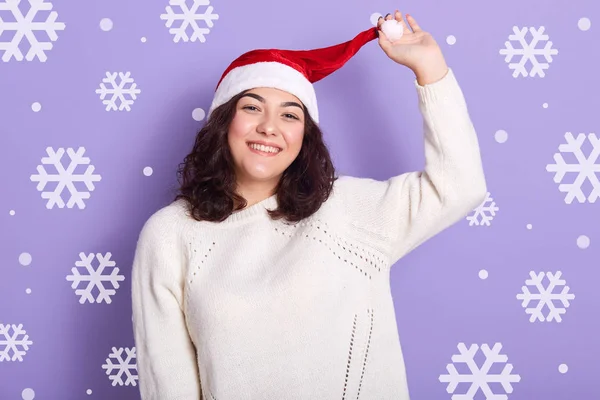 Portrét půvabné brunetky, která se jednou rukou dotýká klobouku, čeká na nový rok, tráví čas sama, užívá si zimních prázdnin, odpočívá, upřímně se usmívá. Koncept dovolené. — Stock fotografie