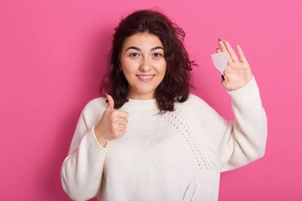 Primer plano retrato de la mujer sosteniendo la copa menstrual aislada sobre fondo púrpura estudio, mujer feliz vistiendo suéter blanco que muestra el pulgar hacia arriba, teniendo período, no le gusta usar servilletas o pampones . — Foto de Stock