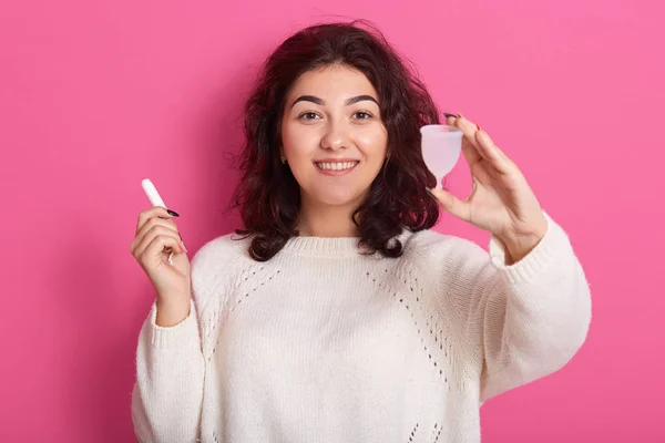 Imagen de la alegre joven enérgica que recomienda usar la copa menstrual durante los días cíticos, sosteniendo el tampón en una mano, de pie aislado sobre fondo rosa en el estudio. Concepto de higiene . — Foto de Stock