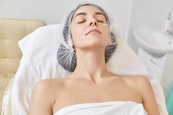Närbild porträtt av ung kvinna tillbringar tid i spa salong för rengöring massage. Modern kosmetologi. Proffesionell kosmetolog. Kvinnliga klänningar medicinsk mössa poserar med slutna ögon medan liggande på couh. — Stockfoto