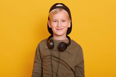 Sarı elbiseli, şapkalı, kulaklık takan, doğrudan kameraya gülümseyen sarı çocuk sarı stüdyo duvarına karşı duruyor. Çocukluk kavramı.