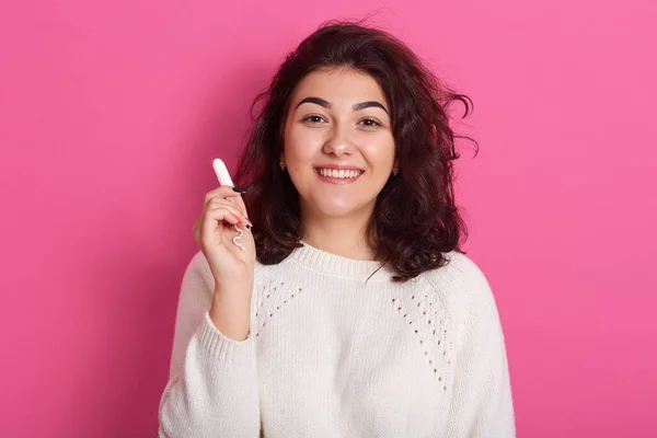 Närbild porträtt av vacker magnetisk brunett tittar direkt på kameran, håller tampong i ena handen, bär vit tröja, har fredliga ansiktsuttryck, gör val. Menstruation begrepp. — Stockfoto