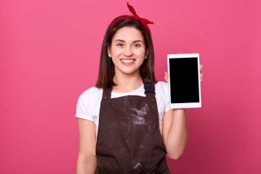 Kapalı bir stüdyoda, mutlu, enerjik, gülümseyen bir kadının bir elinde kapalı tablet, doğrudan kameraya bakan, hoş bir yüz ifadesi olan bir fotoğraf çekimi. Dijital konsept.