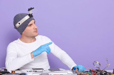 Bilgisayarı tamir eden, jest yapan, kenara bakan, ekipman ve elektronik öğeleri kullanan genç bir elektronik mühendisin yatay resmi. Reklam için eşdeğer alan.