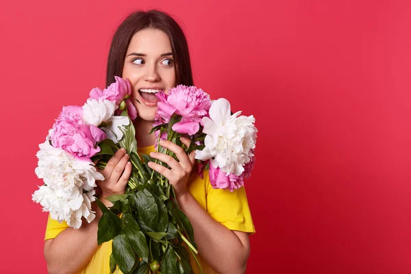 Retrato de divertida dama juguetona feliz sosteniendo ramo de flores blancas y rosadas, vistiendo camiseta amarilla, mirando a un lado, abriendo la boca ampliamente, estando satisfecho con el regalo de San Valentín. Concepto de emociones . — Foto de Stock