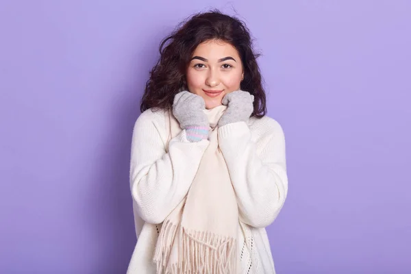 Горизонтальный портрет привлекательной молодой брюнетки, которая кладет руки на шарф, смотрит прямо в камеру, одевается в белую теплую одежду, улыбается, находясь в хорошем настроении. Концепция зимнего отдыха . — стоковое фото