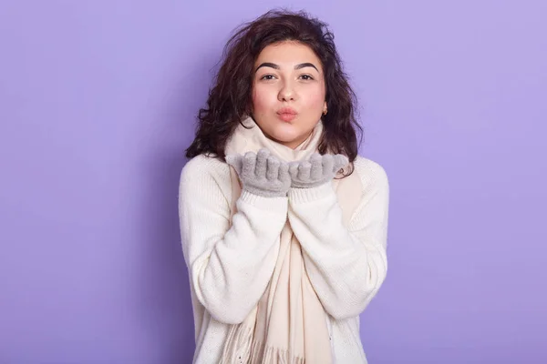 Horizontal foto interior de la morena encantadora emocional? ute de pie aislado sobre fondo lila en el estudio, el uso de suéter blanco y bufanda, guantes grises, poner las manos juntas, enviar un beso . —  Fotos de Stock