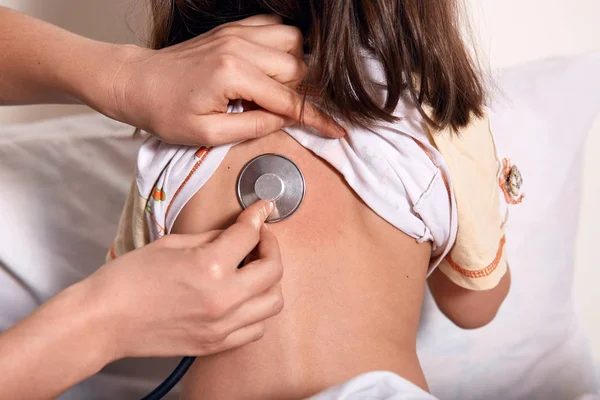 Retrato de cerca del pediatra con el niño paciente en la clínica., mujer de pelo oscuro posando hacia atrás, usando pijama, el médico examina los pulmones de los niños. Diagnóstico, salud, concepto de servicio médico . — Foto de Stock