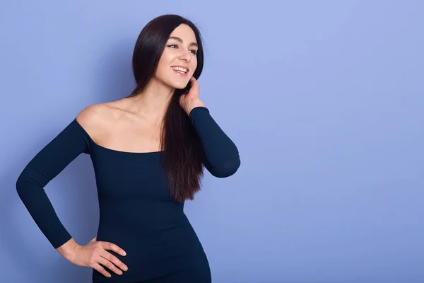 Porträtt av leende söt ung kvinna bär klänning med bara axlar, tittar åt sidan isolerad blå bakgrund i studio. Människor uppriktiga känslor, livsstil koncept. Kopiera utrymme för reklam. — Stockfoto