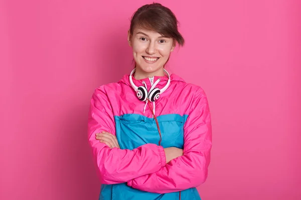 Close-up portret van mooie brunette draagt roze sportshirt gevouwen haar armen over haar borst en direct kijken naar de camera. Lady na fitness, ziet er gelukkig poseren geïsoleerd over roze srudio achtergrond. — Stockfoto