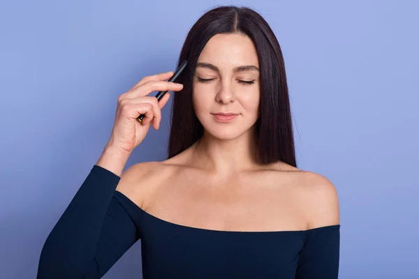 stock image Attractive brunette young model with pefect skin posing with closed eyes wearing trendy dress, keeping fingers near temple, trying to remember important thing, isolated over blue background.