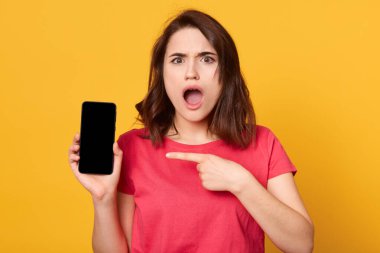Güzel, esmer bir kadının portresi akıllı telefon ekranını gösteriyor ve parmağıyla işaret ediyor, kadın ağzı açık poz veriyor. Alan önleyici reklamını kopyala.