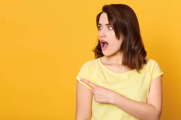 Primer plano retrato de la joven hermosa mujer con camiseta casual, de pie sobre el fondo amarillo aislado y puntos a un lado, se ve preocupado y conmocionado. Copiar espacio para publicidad o texto promocional — Foto de Stock