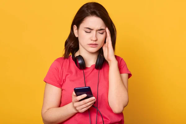 Close up portrait of woman with cellphone isolated over yellow studio background, attarctive female feels headache, young beautiful lady wears casual outfits, keeps eyes closed, touches temple. — 스톡 사진
