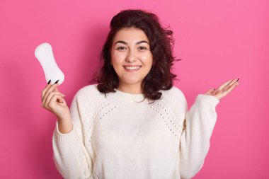 Stüdyoda, sevimli, neşeli, güzel esmer kadının bir elinde hijyen pedi, pembe arka planda izole bir şekilde kameraya bakarken çekilmiş bir fotoğrafı var. Erkekler konsepti.