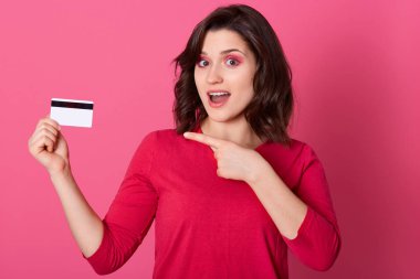 Duygusal açıdan güzel bir bayanın resmi kredi kartını işaret ederek, yüz ifadesini şaşırtarak, ağzını açarak, online alışveriş yaparak. Kadınlar ve satın alma kavramı.