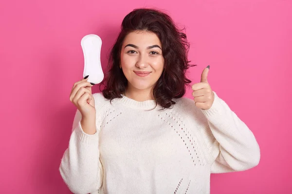Imagen de una mujer rizada sonriente bastante joven haciendo gesto, mostrando un cartel súper, sosteniendo la almohadilla de higiene en una mano, haciendo recomendación, estando encantada, teniendo menstruaciones. Concepto de menstruación . —  Fotos de Stock