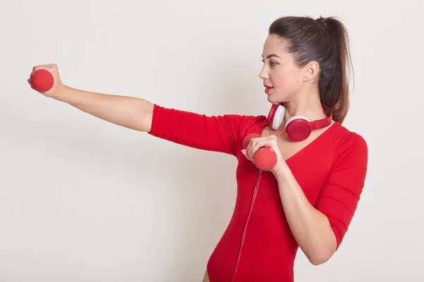 Profile of hard working good looking female doing exercises at sports gym, having ponytail, listening to music while training, keeping fit, spending time alone, losing kilograms. Sport concept. — Stock Photo, Image