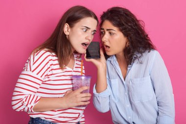 Pembe arka planda cep telefonu kullanan iki güzel kadının, şok edici haberleri duyan çekici kadınların, ağzı açık poz veren mankenlerin yakın portresi. Dedikodu konsepti.