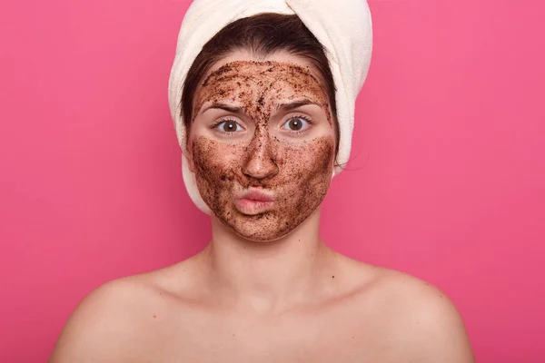 Dissatisfied young woman doesnt like smell from beauty mask, doing procedures for removing wrinkles on face, wearing white towel and standing with bare shoulders isolated over pink studio wall. — Stock Photo, Image