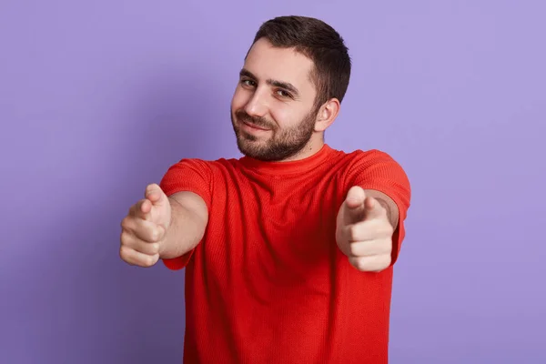 Close up portrait of young attractive man wearing red t shirt pointing at camera isolated purple background, handsome bearded guy looking smiling at camera and pointing with his index fingers. — Stock Photo, Image