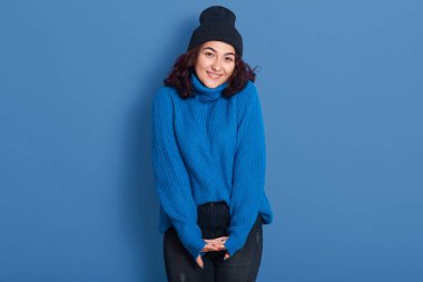 Ellerinin kesiştiği neşeli, pozitif modelin yatay resmi, doğrudan kameraya bakıyor, samimi bir şekilde gülümsüyor, mutlu bir yüz ifadesi takınıyor, günlük giysiler giyiyor. Duygular konsepti.