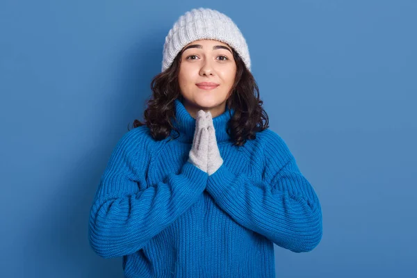 Close up portrait of beautiful brunette woman wearing winter sweater standing isolated over blue background, fascinating lady praying with hands together asks for forgiveness. People emotions concept. — 스톡 사진