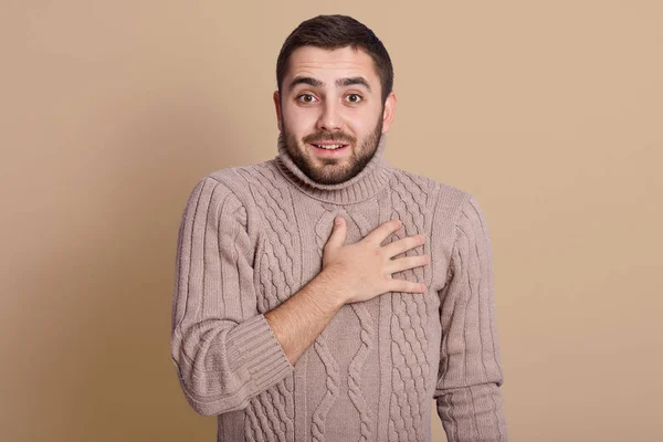 Indoor studio shot of positive energetic young man with black hair, wearing beige sweater, putting hand on chest, looking directly at camera, having peaceful facial expression. Emotions concept. — Stock Photo, Image