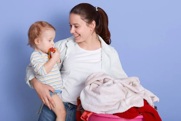 Mother with infant son sitting near laundry basin, mummy looking at her baby with love, cheeper wearing stripped bodysuit nibbles his car toy. Family, adorable kid, love and happiness concept. — Stock Photo, Image